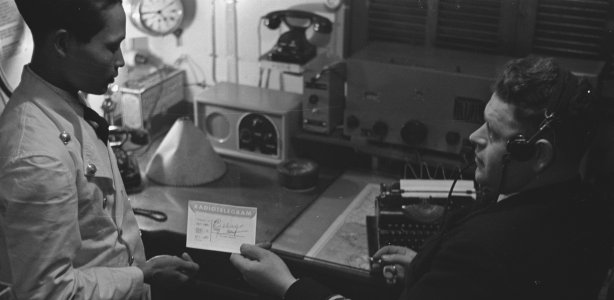 Marconist van een Nederlands koopvaardijschip geeft een bericht aan een Indonesische steward, 1943. (Nationaal Archief) Verdwenen beroep marconist radio-officier telegrafie